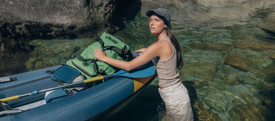 Image of woman canoeing holding a Jeep backpack in the color green.