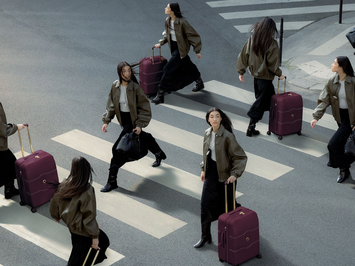 Group of travelers crossing a city street pulling burgundy Delsey suitcases